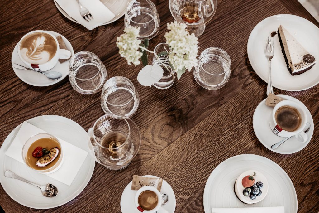detailná záber na stôl s pohármi čistej vody, kvalitným koňakom, espressom a výnimočnými dezertami rôznych tvarov