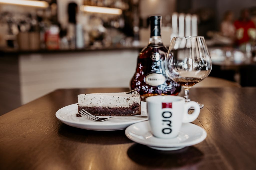 detailný záber na koňak Henessy XO, dezert z patisserie a espresso v šálke Caffe Oro