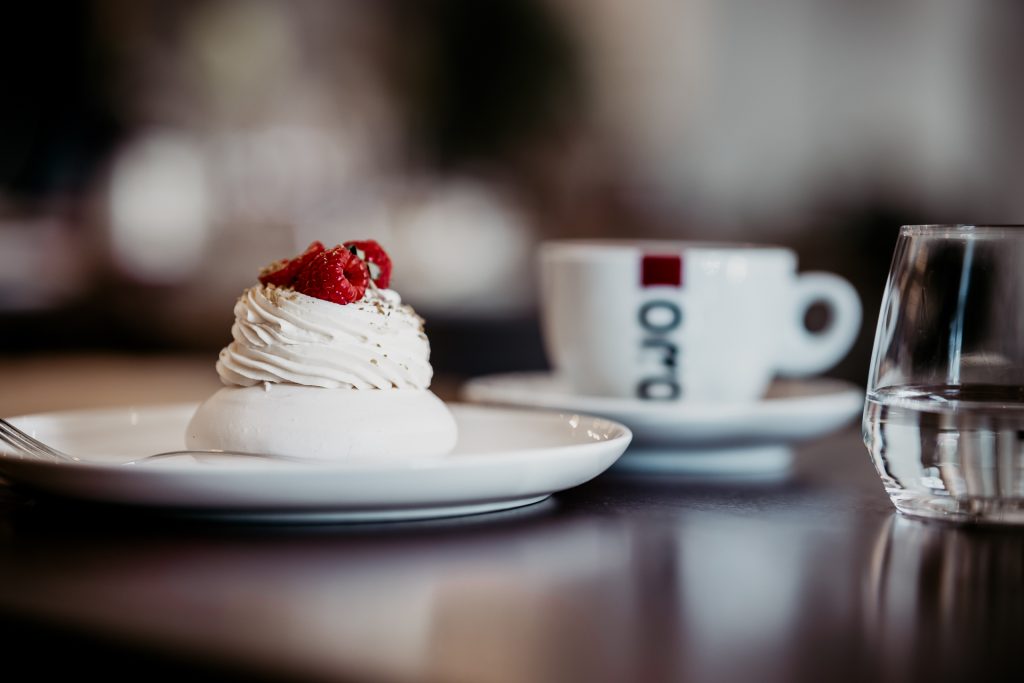 detail dezertu Pavlova tortička, v pozadí espresso ORO a pohár vody