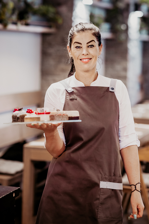 čašníčka s táckou plnou francúzskych dezertov, v pozadí interiér reštaurácie